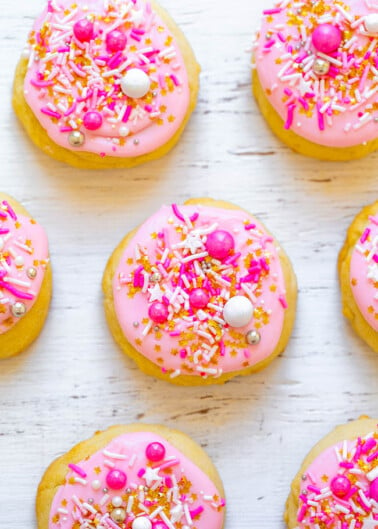 Pink frosted cookies with colorful sprinkles arranged on a white surface.