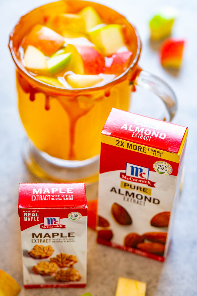 Maple extract and almond extract in front of glass of caramel apple cider. 