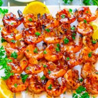 Grilled shrimp skewers garnished with parsley and lemon slices served on a white plate.