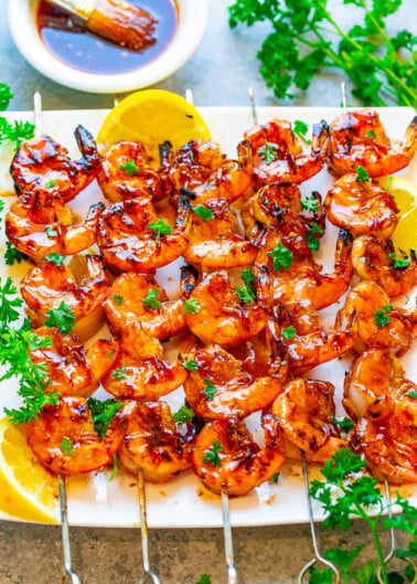 Grilled shrimp skewers garnished with parsley and lemon slices on a plate.
