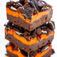 Stack of chocolate brownies with orange cream layers and cookie pieces.
