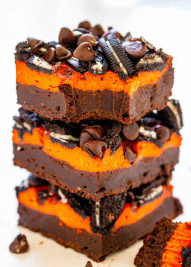Stack of layered brownies with orange cream and chocolate chips garnished with cookie pieces.