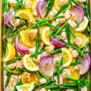 A tray of seasoned chicken, green beans, red onions, and lemon slices ready for roasting.