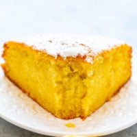 A slice of lemon cake dusted with powdered sugar on a white plate.