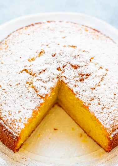 A freshly baked sponge cake with a dusting of powdered sugar and one slice removed.