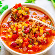 A bowl of colorful chili with ground meat, beans, corn, and diced tomatoes, garnished with fresh cilantro.