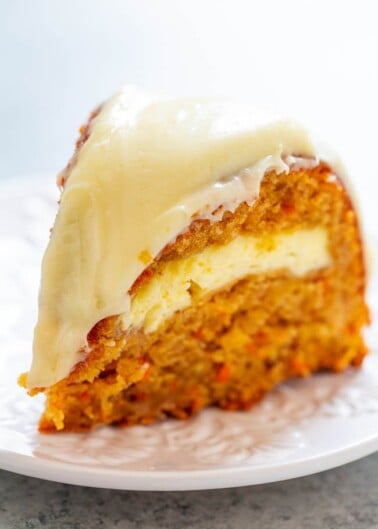 A slice of carrot cake with cream cheese frosting on a white plate.