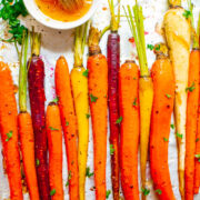 Roasted multicolored carrots arranged on a baking sheet with a brush and herb garnish.