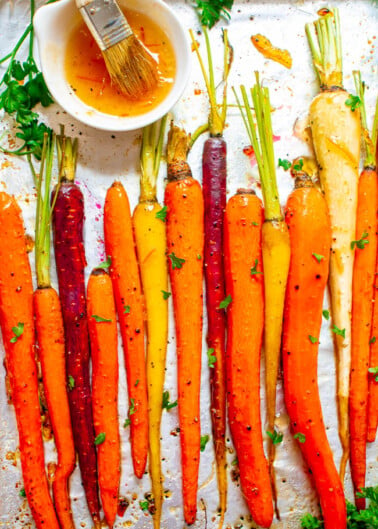 Roasted multicolored carrots arranged on a baking sheet with a brush and herb garnish.