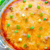 Baked cheese dip garnished with green onions in a glass dish, accompanied by tortilla chips.