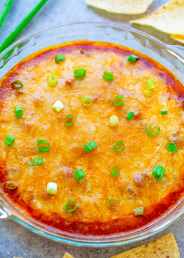 A baked cheese dip garnished with green onions, served with tortilla chips.