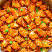 Sesame chicken with sauce and green onions in a cooking pot.