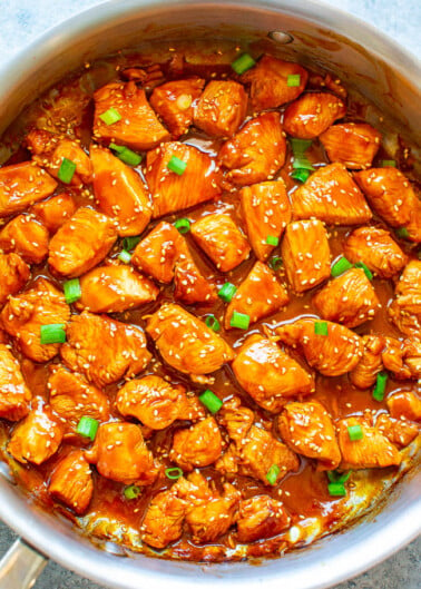 Sesame chicken with sauce and green onions in a cooking pot.