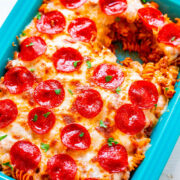 Baked pepperoni pizza casserole in a blue dish, garnished with fresh herbs.