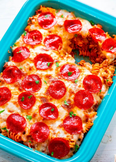 Baked pepperoni pizza casserole in a blue dish, garnished with fresh herbs.