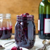 A jar of homemade jam on a rustic table with a bottle of wine in the background.