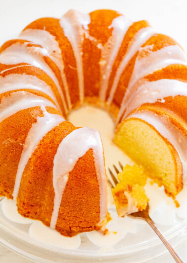 A sliced bundt cake with white glaze on a glass serving plate with a fork.