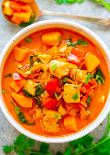 A bowl of colorful chicken and vegetable stew garnished with fresh herbs.