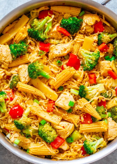 Stir-fried noodles with chicken, broccoli, baby corn, and red pepper in a pan.