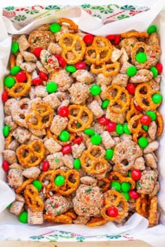 A colorful mix of puppy chow, pretzels, and red and green candies in a festive bowl.