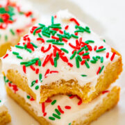 Sliced sugar cookies with white icing and red and green sprinkles, one partially eaten.