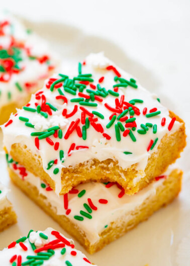Sliced sugar cookies with white icing and red and green sprinkles, one partially eaten.