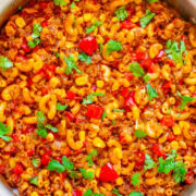 Pot of homemade goulash with macaroni, tomatoes, and ground meat, garnished with fresh parsley.