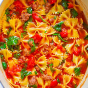 A pot of bow-tie pasta with ground meat, spinach, and tomatoes.