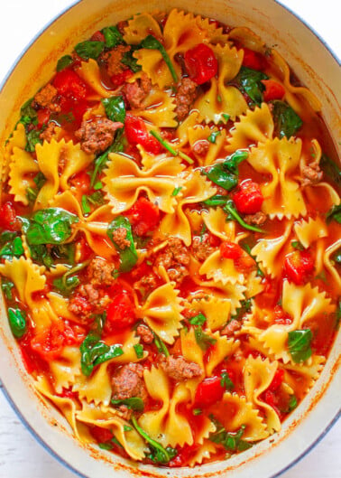 A pot of bow-tie pasta with ground meat, spinach, and tomatoes.