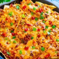A skillet loaded with baked nachos topped with cheese, ground meat, beans, and garnished with green onions.