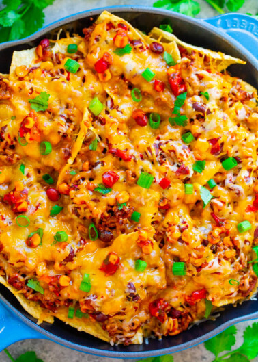 A skillet of baked nachos topped with melted cheese, beans, ground meat, and sliced green onions.