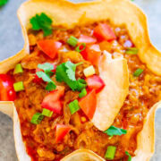 A homemade taco salad in a crispy tortilla bowl garnished with fresh tomatoes, green onions, and cilantro.