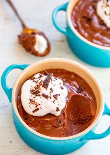 Two bowls of chocolate mousse garnished with whipped cream and chocolate shavings.