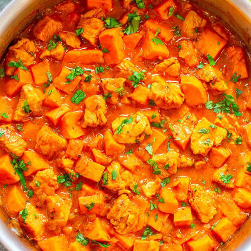 A pot of hearty chicken and potato stew garnished with fresh herbs.