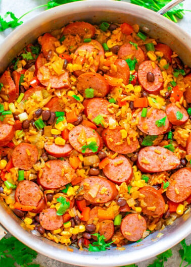 A bowl of colorful rice dish with sausage slices, corn, beans, and diced vegetables.