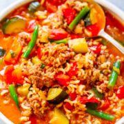 A bowl of hearty stew with ground meat, rice, and mixed vegetables in a tomato-based broth.