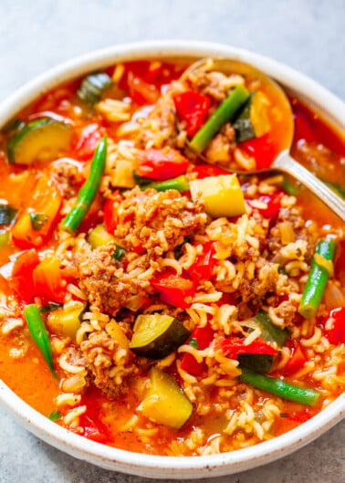 A bowl of hearty stew with ground meat, rice, and mixed vegetables in a tomato-based broth.