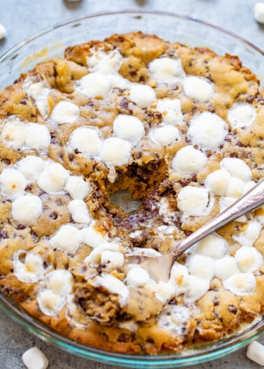 Freshly baked cookie pie with marshmallows, served in a glass dish with a spoon.