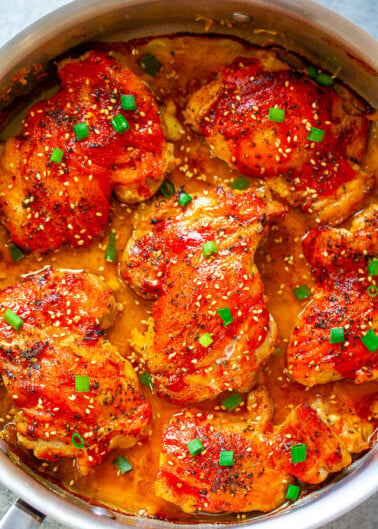 Glazed chicken thighs sprinkled with sesame seeds and chopped green onions in a cooking pan.