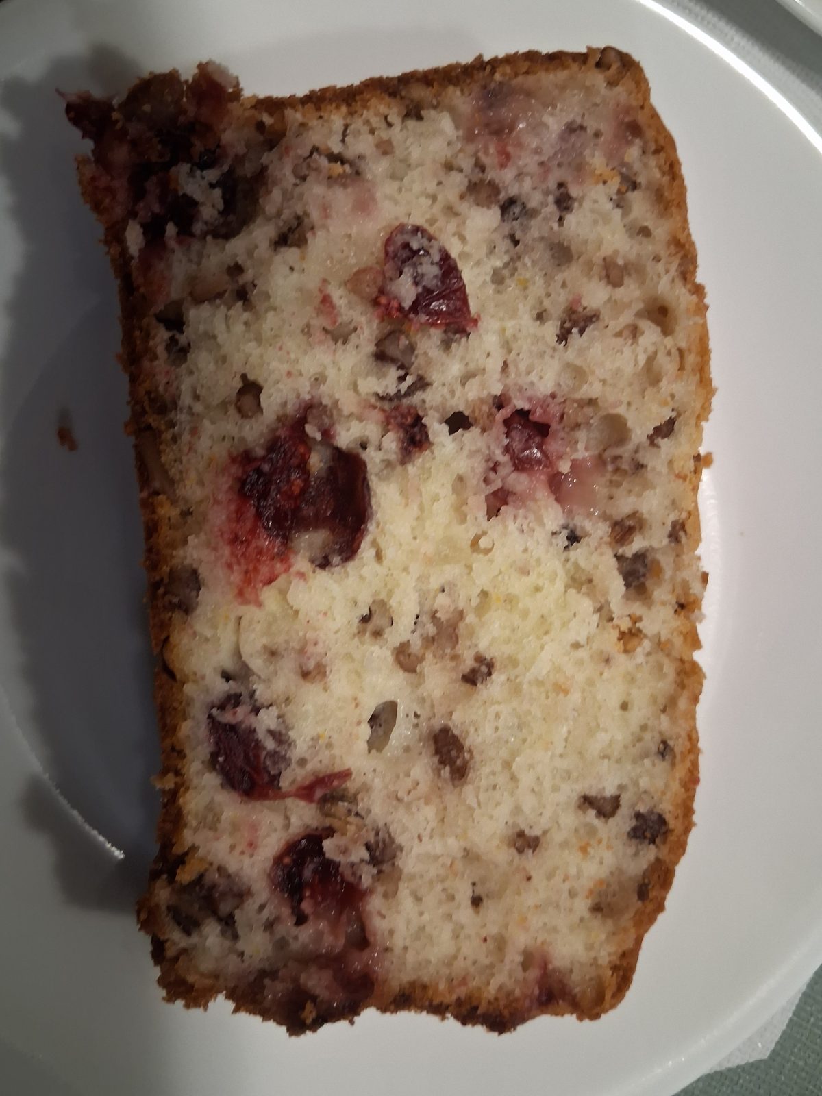 A slice of baked bread with visible pieces of nuts and berries on a white plate.
