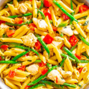 A colorful skillet of penne pasta mixed with vegetables and chicken pieces.