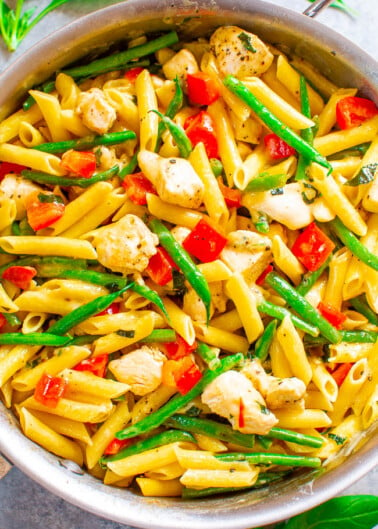 A colorful skillet of penne pasta mixed with vegetables and chicken pieces.