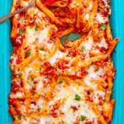 Baked ziti with melted mozzarella cheese in a blue dish, garnished with herbs.