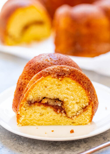 A slice of marble bundt cake on a white plate with the remaining cake in the background.