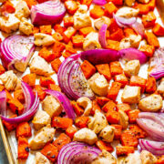 Diced chicken, red onions, and bell peppers seasoned and spread out on a baking sheet.