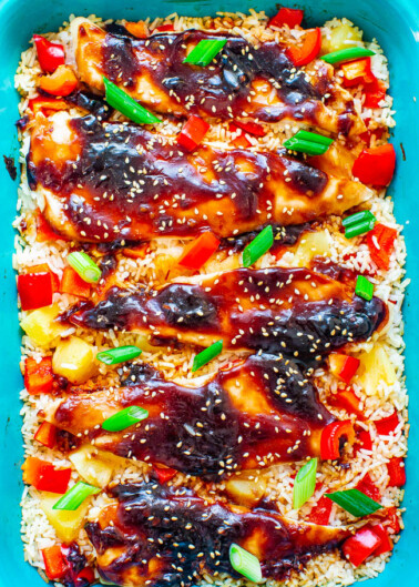 Baked teriyaki chicken over rice garnished with sesame seeds and green onions in a blue dish.