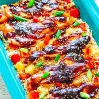 Baked chicken with a teriyaki glaze over rice with diced vegetables and sesame seeds in a blue dish.