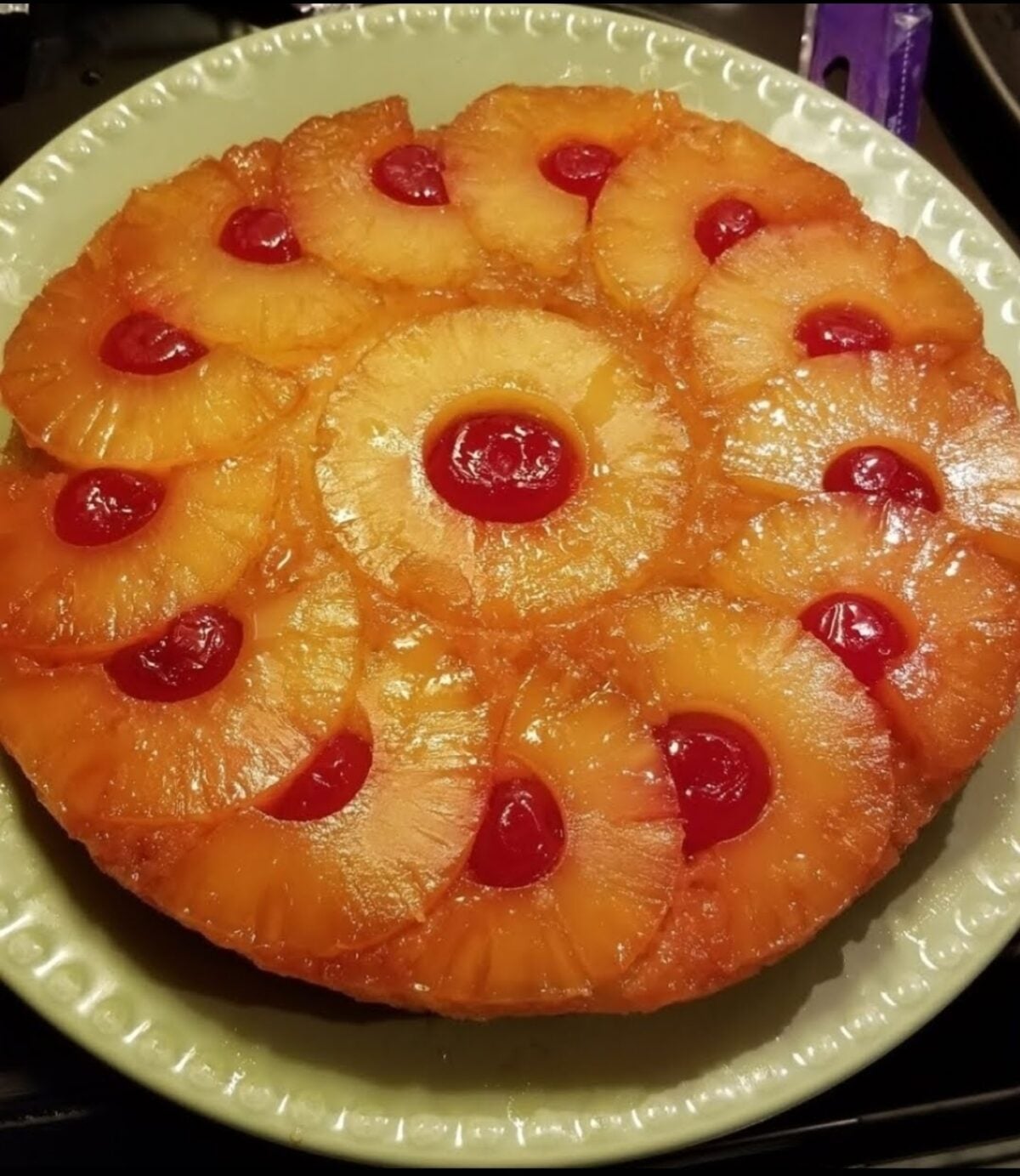 A pineapple upside-down cake with rings of pineapple and cherries on a white plate.