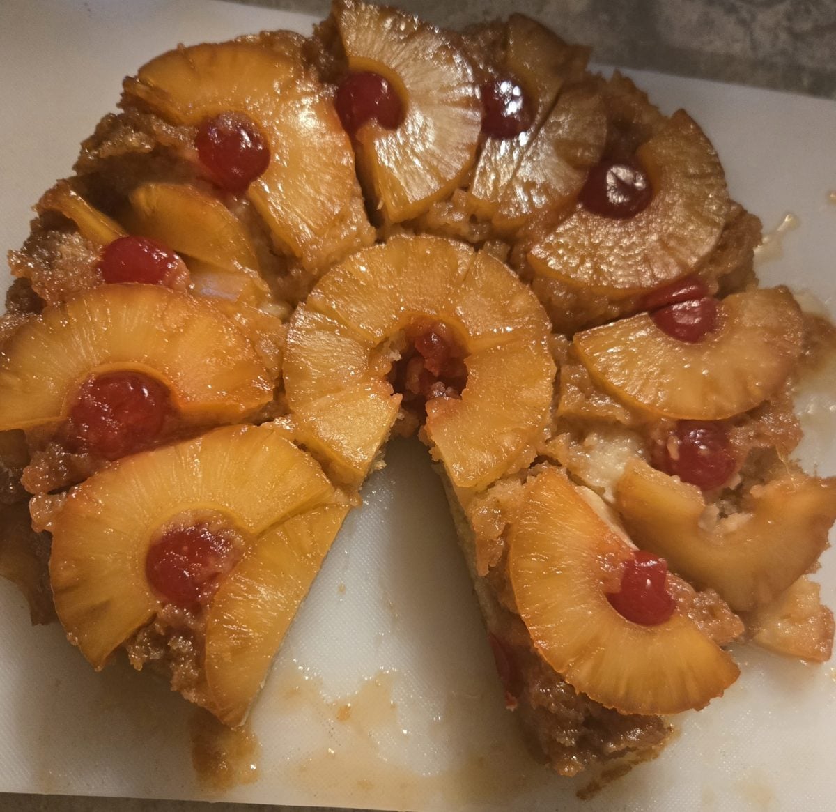 A pineapple upside-down cake topped with pineapple rings and maraschino cherries, with one slice missing from the round cake.