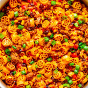 A pot of spicy wheel-shaped pasta with ground meat, beans, and vegetables, garnished with chopped green onions.